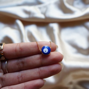 Peut inclure: Un collier en cha&icirc;ne dor&eacute;e avec un pendentif bleu en forme d'&oelig;il mal&eacute;fique. Le pendentif a un centre blanc et une bordure dor&eacute;e.