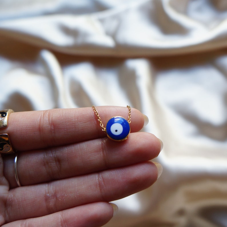 Peut inclure: Un collier en cha&icirc;ne dor&eacute;e avec un pendentif bleu en forme d'&oelig;il mal&eacute;fique. Le pendentif a un centre blanc et une bordure dor&eacute;e.
