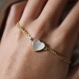 May include: A gold chain bracelet with a white heart-shaped charm.