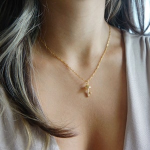 Puede incluir: Un delicado collar dorado con un peque&ntilde;o colgante de llave. El colgante de llave tiene detalles intrincados y cuelga de una fina cadena. El collar se usa sobre un fondo neutro.