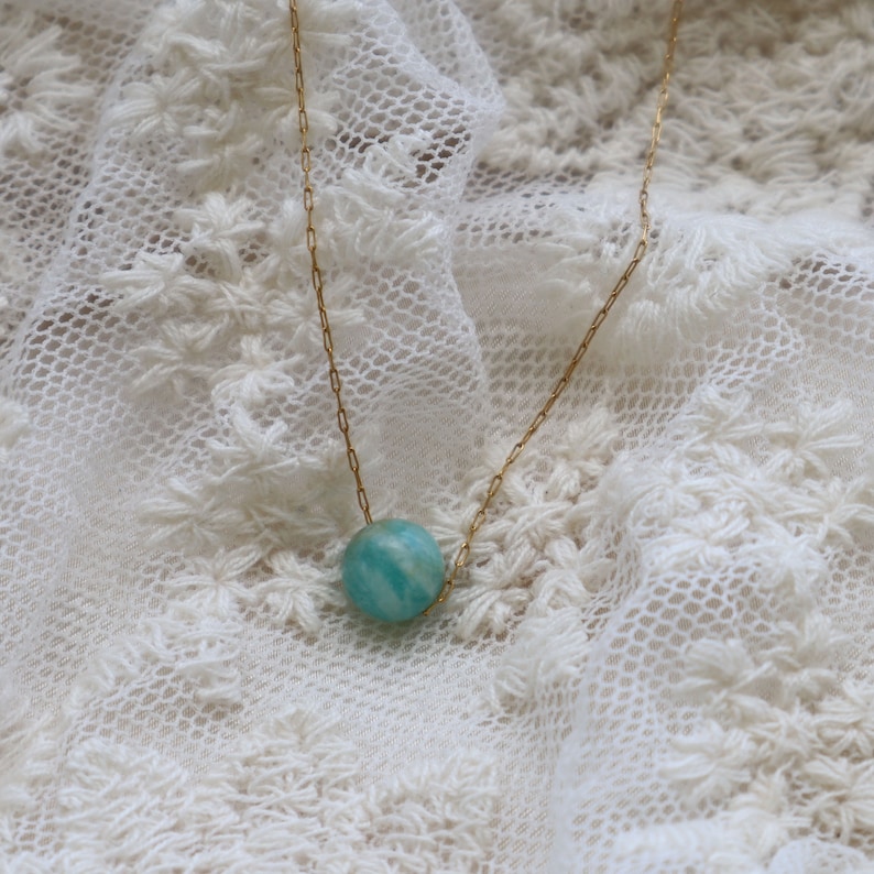 May include: A gold chain necklace with a single round blue-green gemstone pendant.