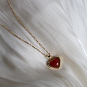 May include: A gold chain necklace with a heart-shaped pendant. The pendant has a red gemstone in the center.