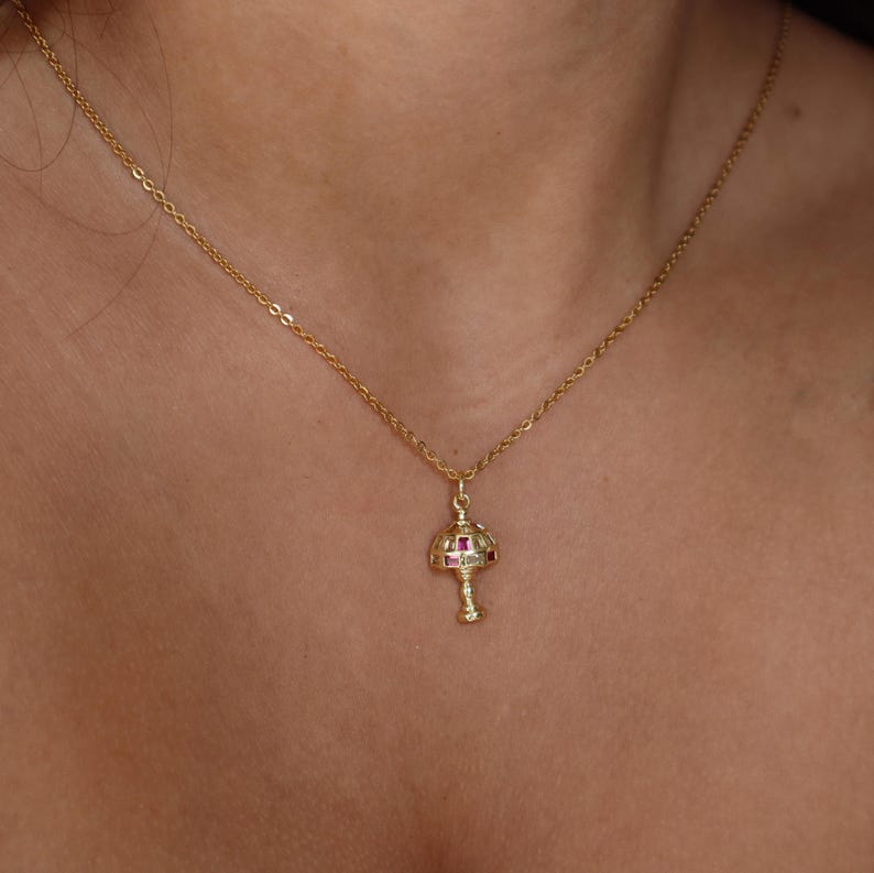 May include: A gold chain necklace with a pendant shaped like a lamp with red gemstones.