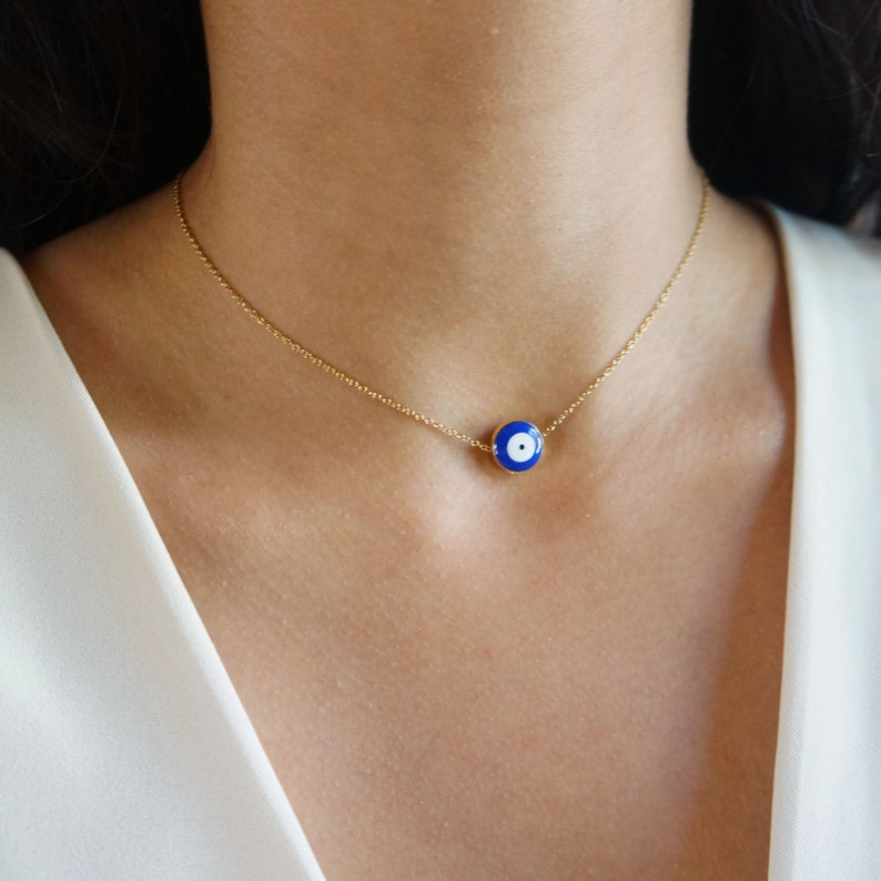 Peut inclure: Un collier en cha&icirc;ne dor&eacute;e avec un pendentif &oelig;il turc bleu et blanc. Le pendentif est rond et a un centre blanc avec un cercle bleu autour.