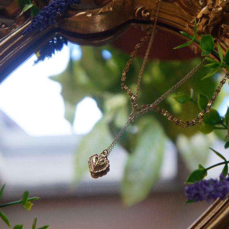 May include: A gold necklace with a heart-shaped pendant. The pendant has a detailed design and is hanging from a delicate chain.