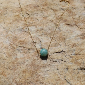 May include: A gold chain necklace with a single round teal gemstone pendant.