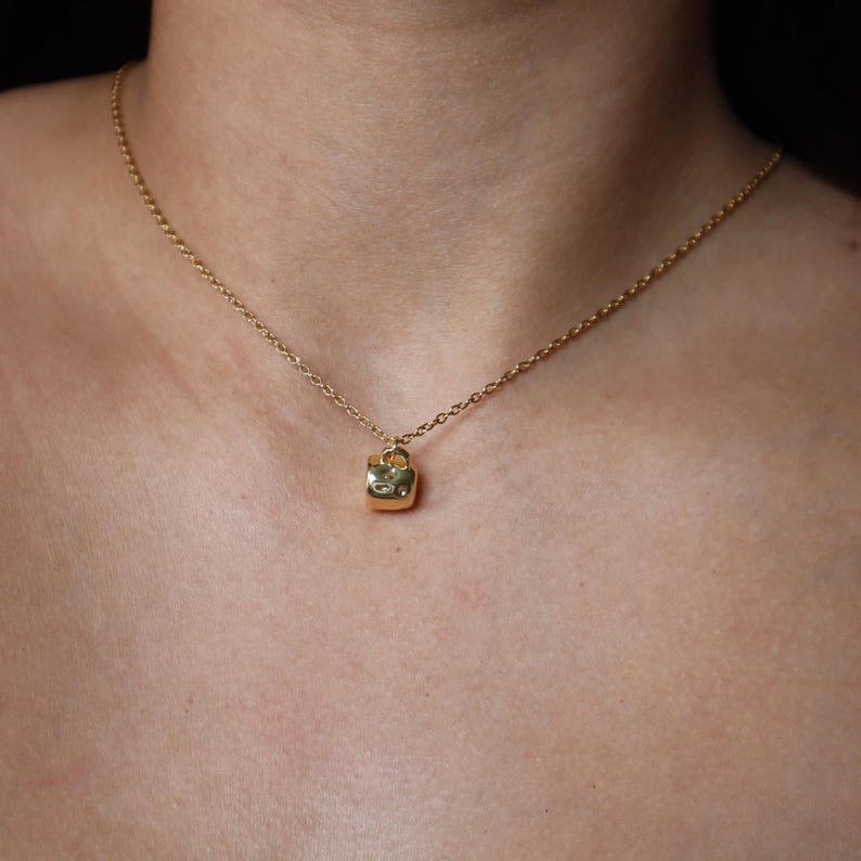 May include: A gold chain necklace with a small, square pendant shaped like a padlock.