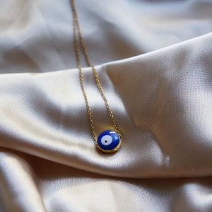Peut inclure: Un collier en cha&icirc;ne dor&eacute;e avec un pendentif &oelig;il turc bleu et blanc. Le pendentif est rond et a une bordure dor&eacute;e.