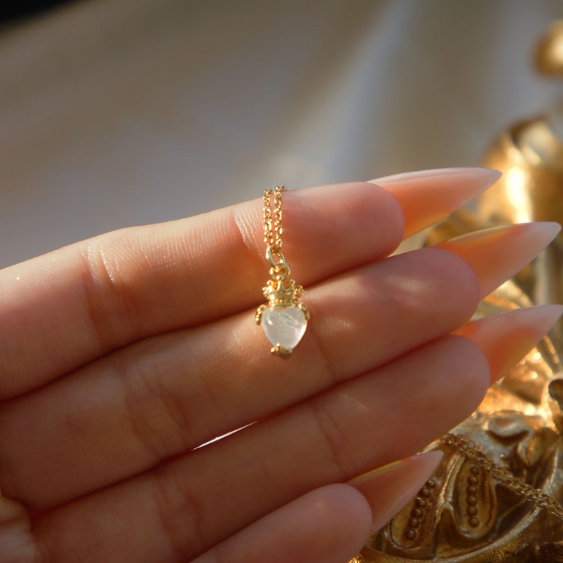 May include: A gold necklace with a white heart-shaped pendant topped with a crown.