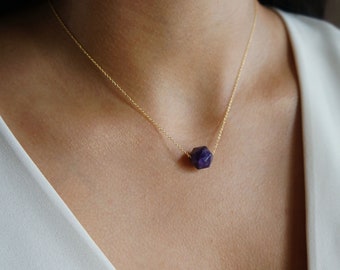 May include: A gold chain necklace with a single, faceted, purple gemstone pendant.