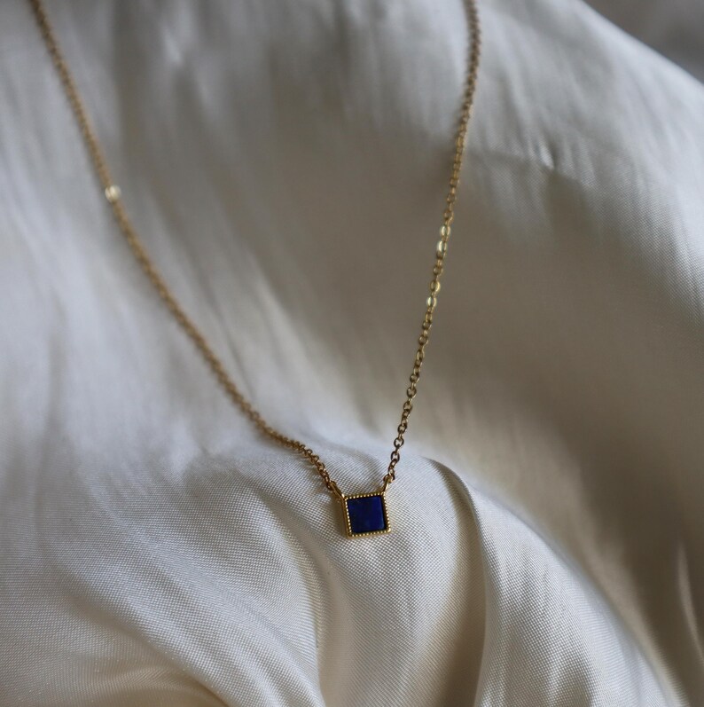 Peut inclure: Un collier en cha&icirc;ne dor&eacute;e avec un petit pendentif carr&eacute; orn&eacute; d'une pierre pr&eacute;cieuse bleu fonc&eacute;.