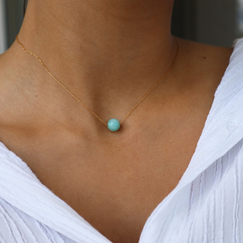 May include: A delicate gold chain necklace with a single, round turquoise gemstone pendant.