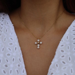 Puede incluir: Un collar de cadena de oro con un colgante de cruz de perlas y piedras preciosas.