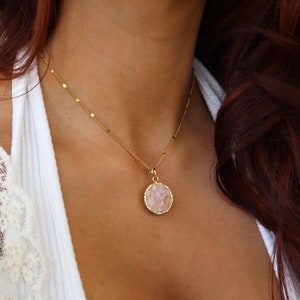 May include: A gold chain necklace with a round pendant featuring a pink crystal.