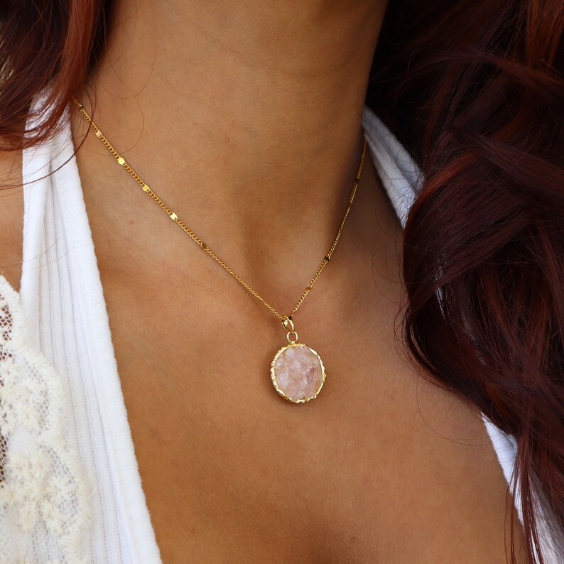 May include: A gold chain necklace with a round pendant featuring a pink crystal.