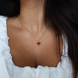 May include: A gold chain necklace with a red heart pendant. The heart is outlined in gold and has a slightly raised surface.
