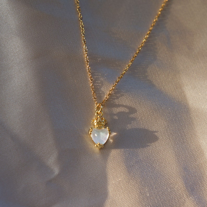 May include: A gold necklace with a heart-shaped pendant featuring a white stone and a crown design.