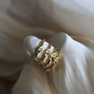 May include: Four gold rings with a single clear stone on each. The rings are stacked on top of each other and have a wavy, organic design.