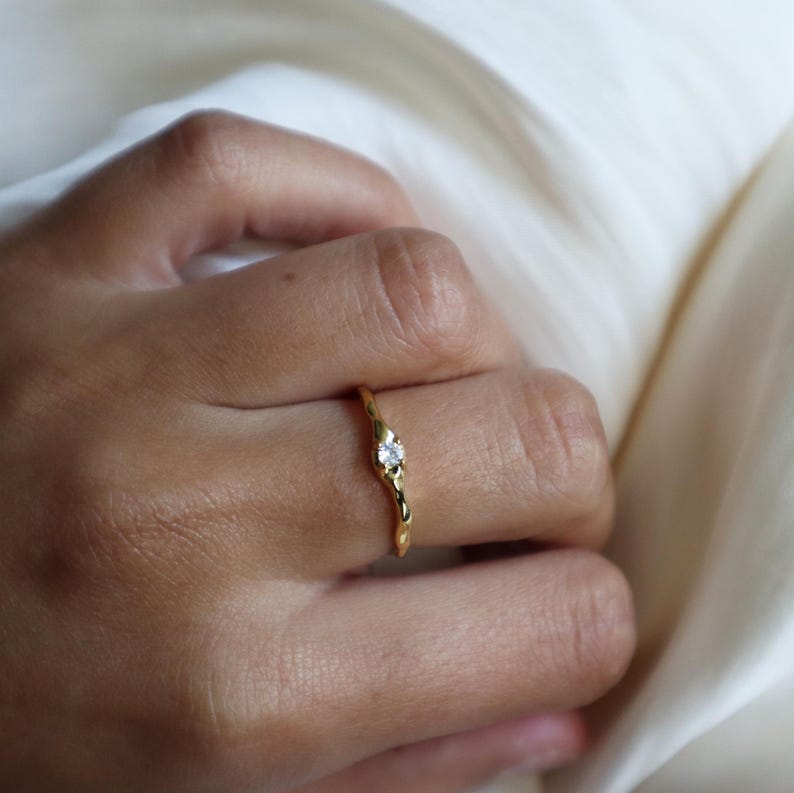 May include: A gold ring with a textured band and a small, clear gemstone.