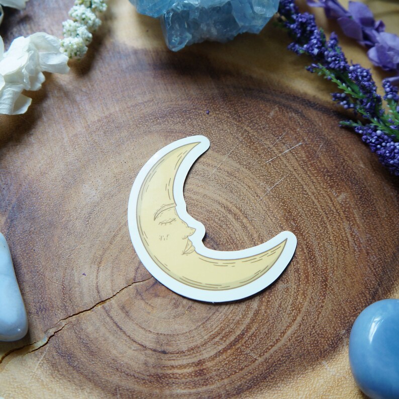 May include: A yellow crescent moon sticker with a sleeping face on a wooden surface.