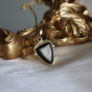 May include: A gold necklace with a black triangular pendant featuring a shimmering, iridescent stone.