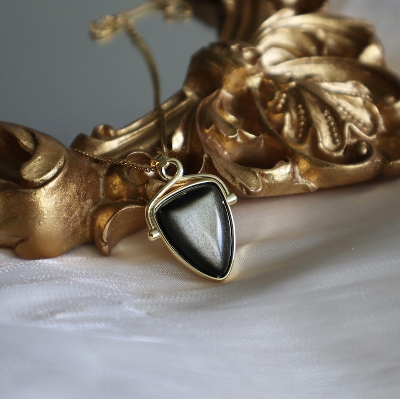 May include: A gold necklace with a black triangular pendant featuring a shimmering, iridescent stone.