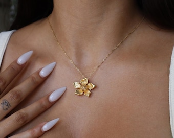 May include: A gold flower pendant necklace with a delicate chain. The flower pendant has a textured surface and a round center.