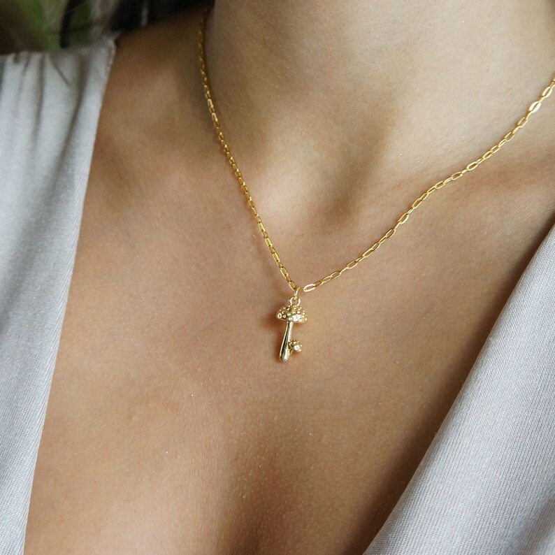 Puede incluir: Un collar dorado con un colgante de llave. El colgante de llave est&aacute; adornado con peque&ntilde;os detalles brillantes. El collar se muestra en el pecho de una persona, destacando el dise&ntilde;o y el estilo de la joya.