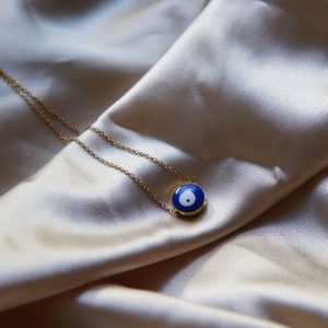 Peut inclure: Un collier en cha&icirc;ne dor&eacute;e avec un pendentif &oelig;il turc bleu et blanc. Le pendentif est rond et a un cercle blanc au centre de l'&oelig;il bleu.