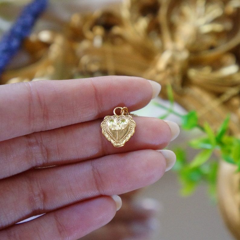 May include: A gold heart-shaped pendant necklace with a detailed design. The pendant features a small, raised design inside the heart.