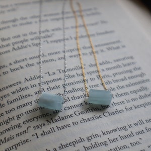 May include: Three delicate necklaces with light blue gemstone beads. The necklaces are layered on a book with text visible in the background.