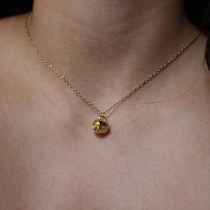 May include: A gold chain necklace with a small gold cup pendant.