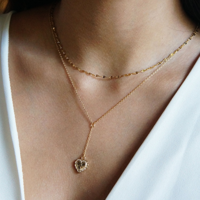 May include: A gold chain necklace with a delicate heart pendant. The necklace is layered with a shorter chain.