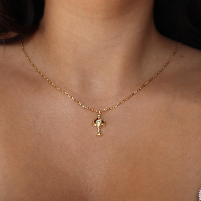 May include: A gold chain necklace with a small, detailed pendant shaped like a mushroom with red accents.