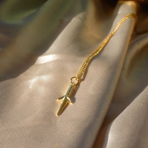 Puede incluir: Un collar de cadena de oro con un peque&ntilde;o colgante de daga de oro.