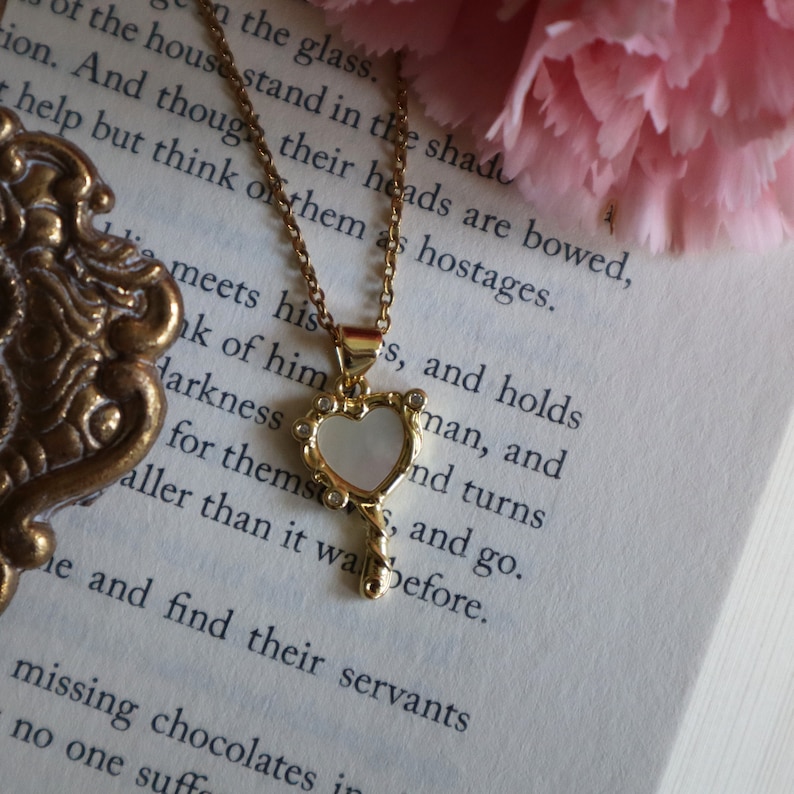 May include: A gold necklace with a heart-shaped pendant featuring a white mother-of-pearl inlay and clear rhinestones. The pendant is shaped like a key.