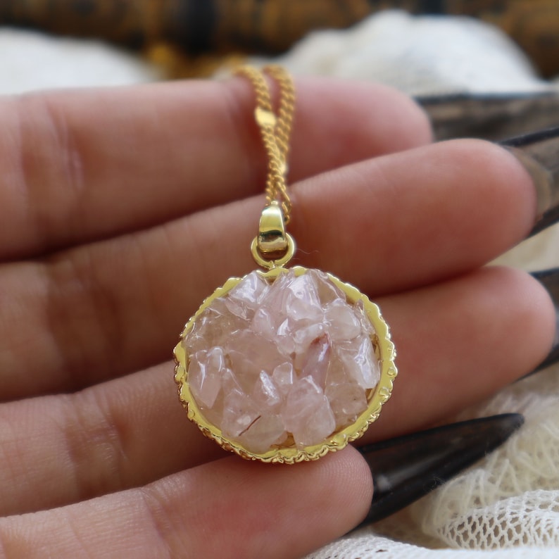 May include: A gold chain necklace with a round pendant featuring a cluster of pink rose quartz crystals.