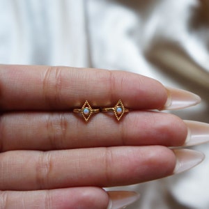 May include: A pair of gold earrings with a diamond shape and a small opal stone in the center.