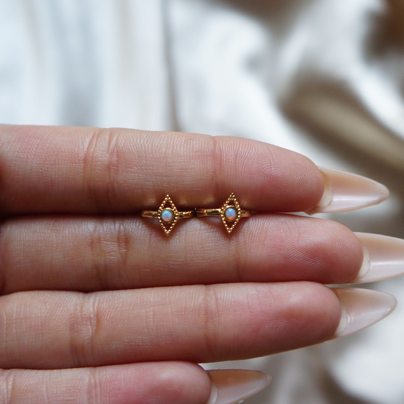 May include: A pair of gold earrings with a diamond shape and a small opal stone in the center.