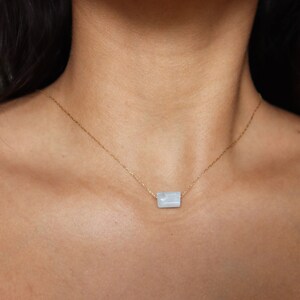 May include: A delicate gold chain necklace with a light blue rectangular pendant. The pendant has a subtle marbled pattern.
