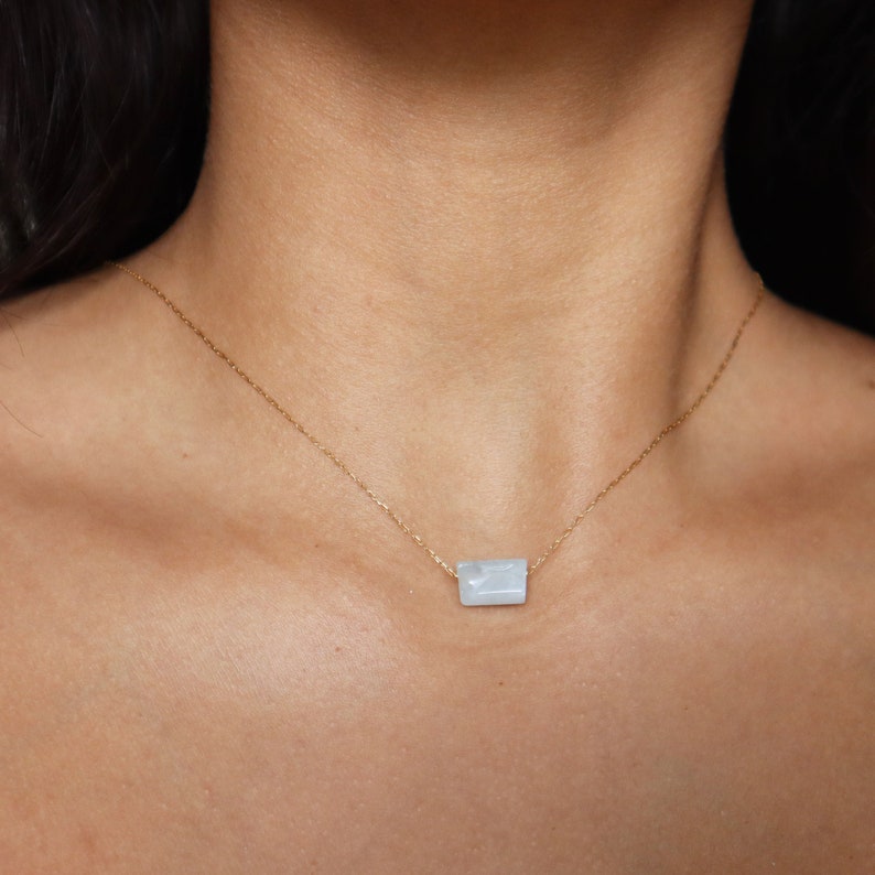 May include: A delicate gold chain necklace with a light blue rectangular pendant. The pendant has a subtle marbled pattern.