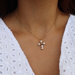 Puede incluir: Un collar de cadena dorada con un colgante de cruz de perlas. La cruz est&aacute; hecha de peque&ntilde;as perlas que rodean una peque&ntilde;a piedra oscura.