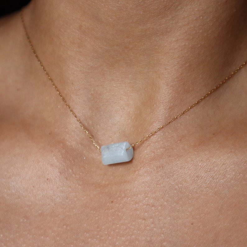 May include: A delicate gold chain necklace with a light blue gemstone pendant. The pendant is a rectangular shape with slightly rounded edges.