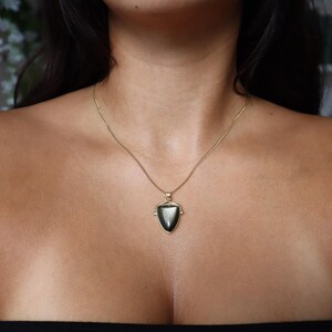 May include: A gold chain necklace with a black gemstone pendant in the shape of a triangle.