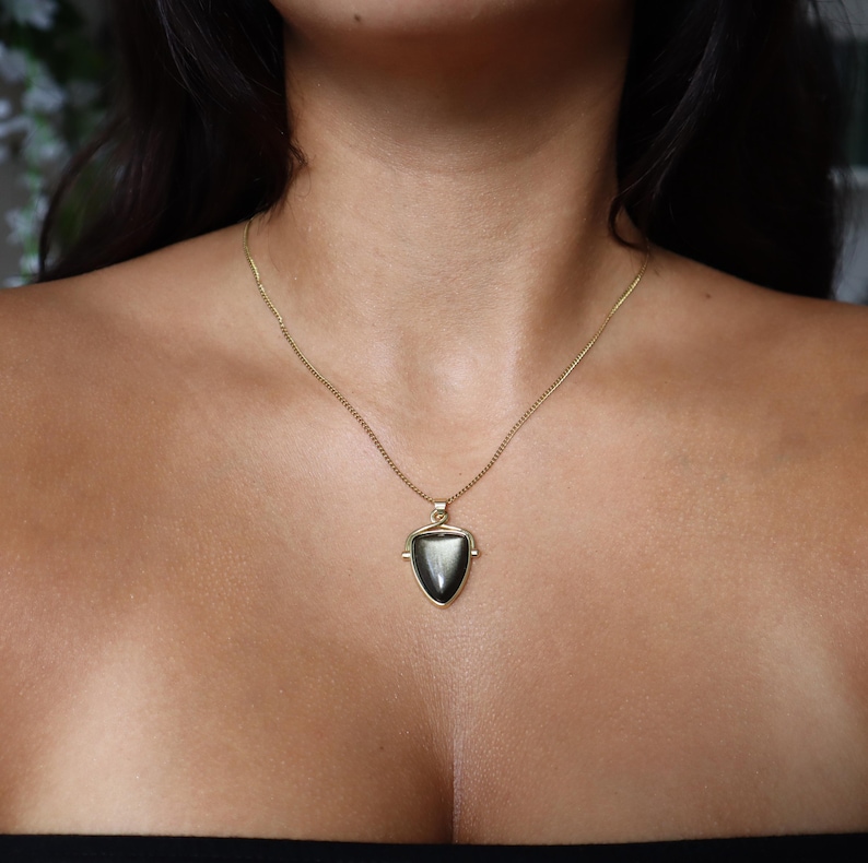 May include: A gold chain necklace with a black gemstone pendant in the shape of a triangle.