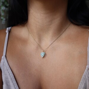 May include: A delicate gold chain necklace featuring a pale blue-green gemstone pendant. The pendant is a rough, irregular shape, and the necklace is displayed against a neutral background.