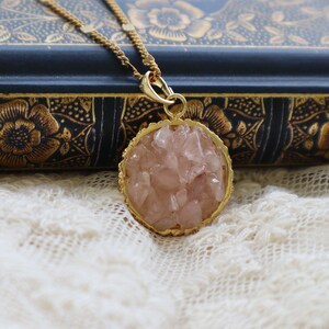 May include: A gold necklace with a round pendant featuring a cluster of pink rose quartz crystals.