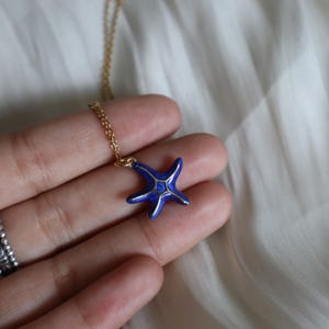 May include: A gold chain necklace with a blue enamel starfish pendant. The starfish has gold accents.