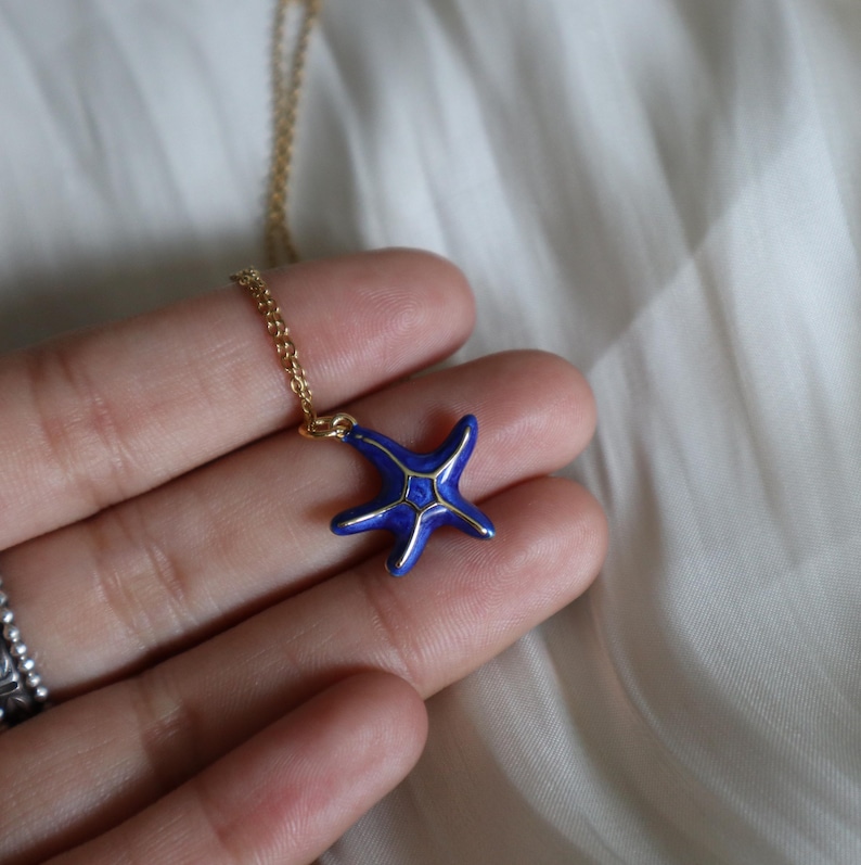 May include: A gold chain necklace with a blue enamel starfish pendant. The starfish has gold accents.