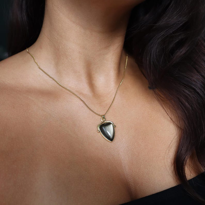 May include: A gold chain necklace with a black and white gemstone pendant in the shape of a triangle.